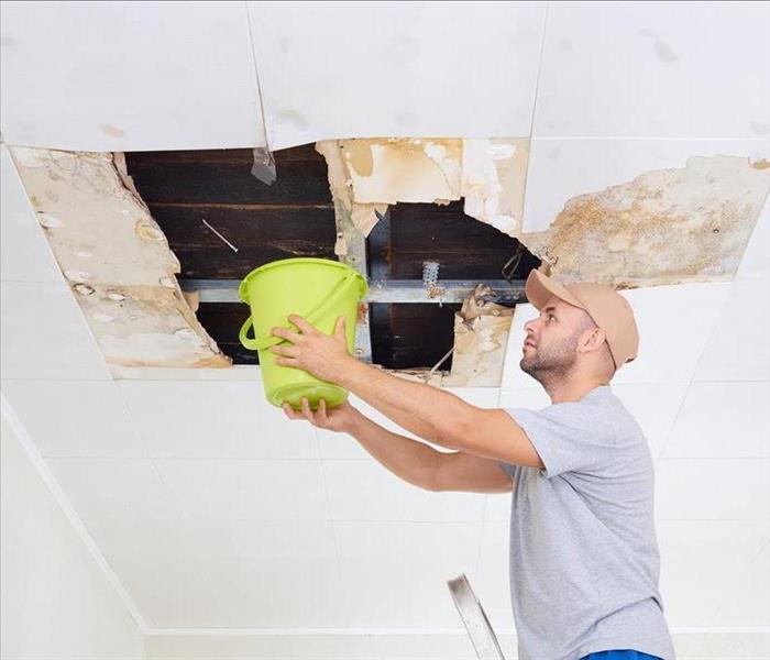 Image of a ceiling leaking water and a person holding a bucket 