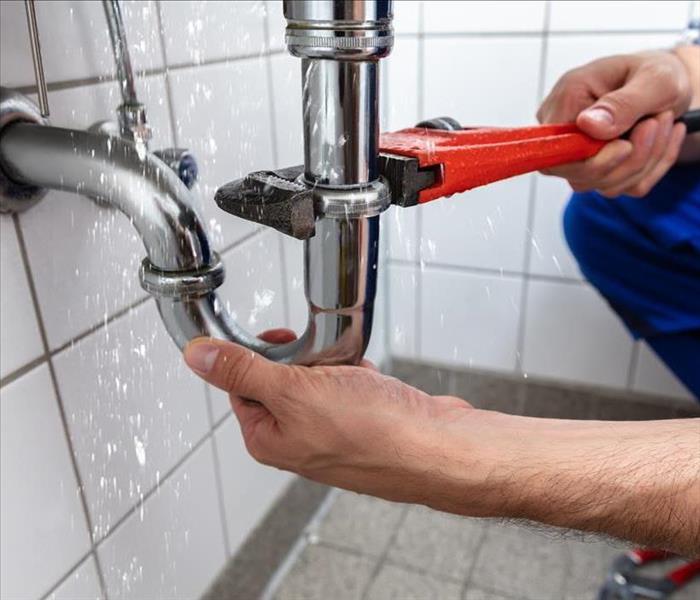 Image of a person fixing a leaking pipe.